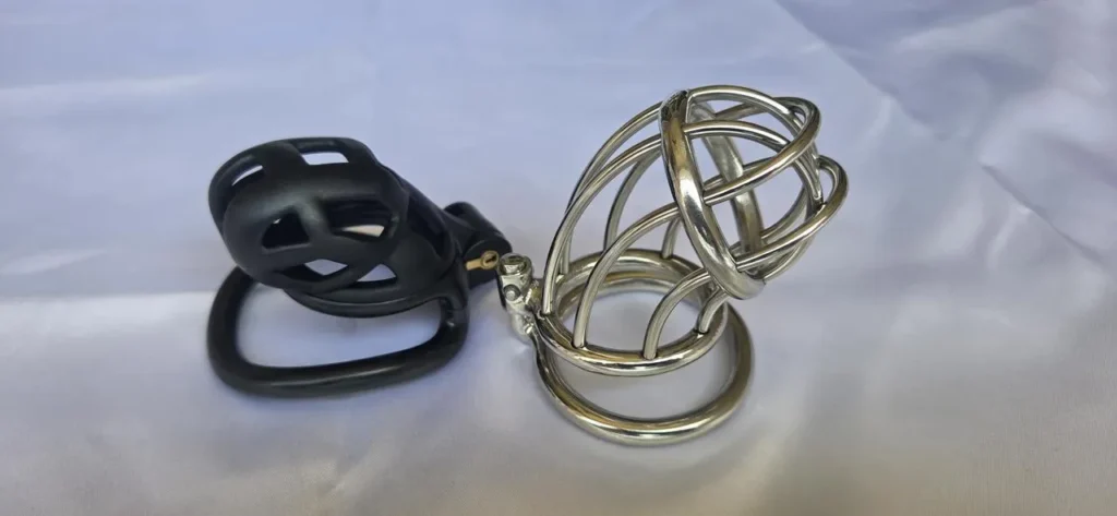 Black silicone chastity cage beside a stainless steel open bar chastity cage and base ring.