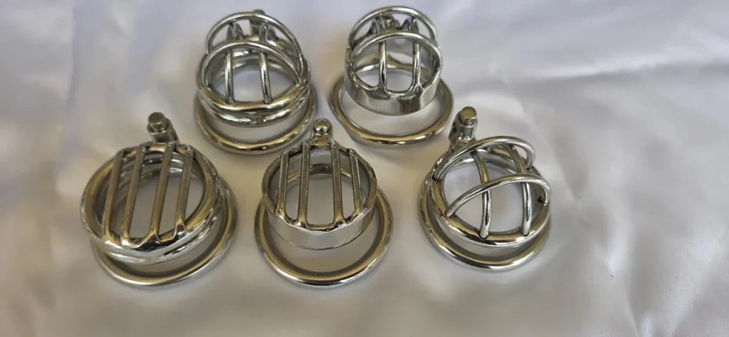 Five short stainless steel chastity cages photographed front-on with their base rings